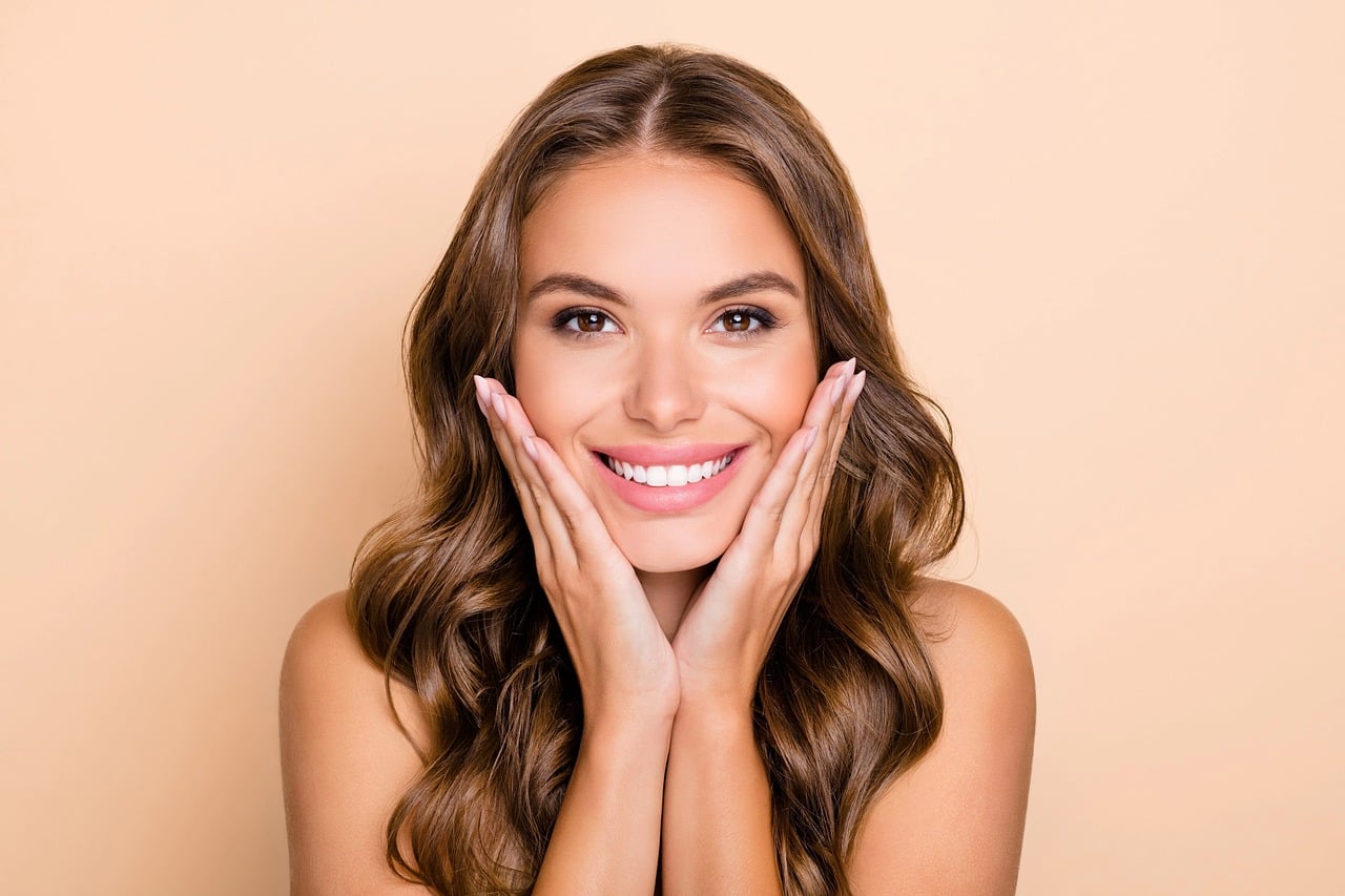 A smiling woman with clear skin, hands framing her face