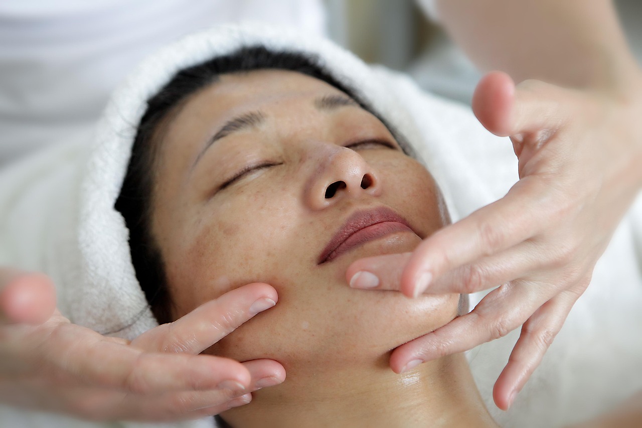 A client wrapped in a white towel having a facial, hands at her jaw