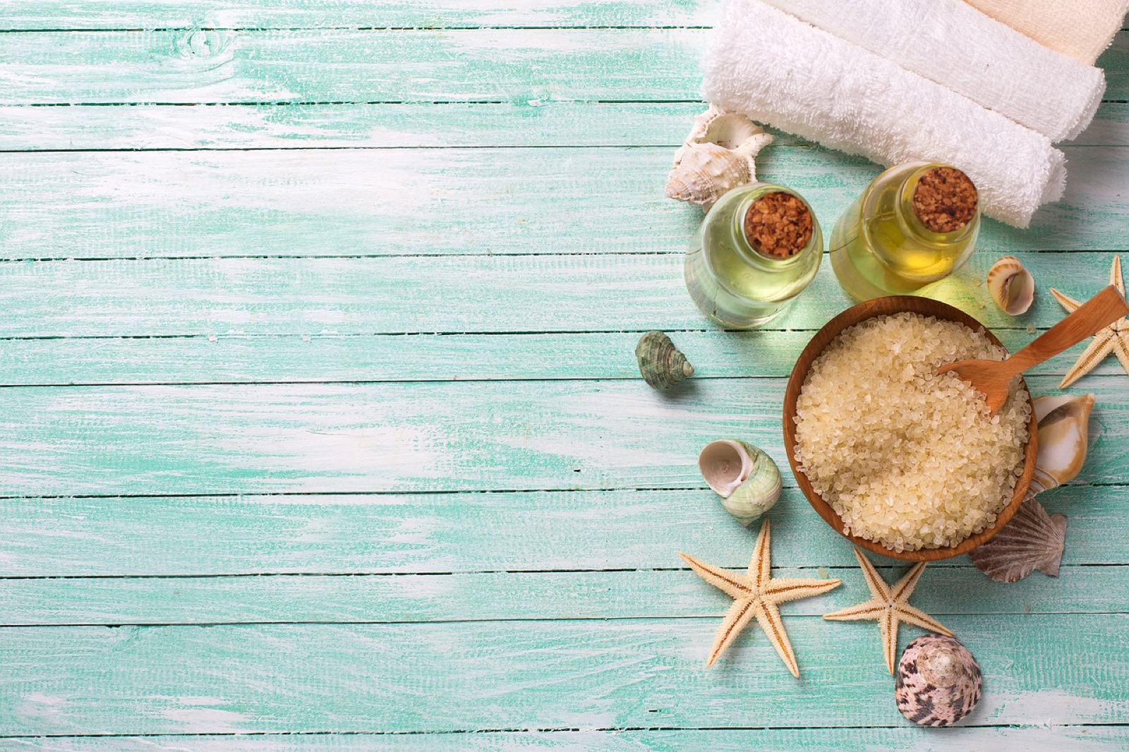 Rolled white towels, oils and bath salts on pale aqua boards
