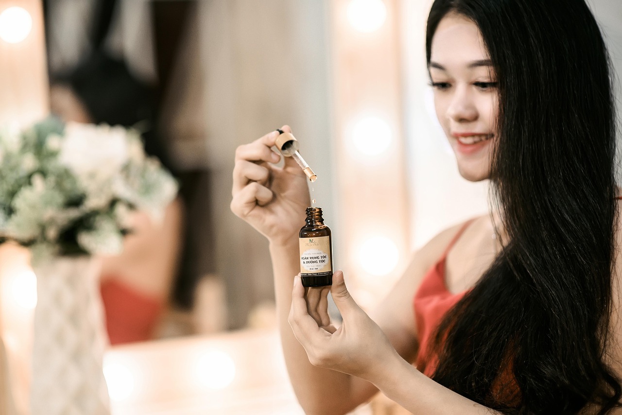 A woman holding up a small dropper bottle of serum at a lit mirror